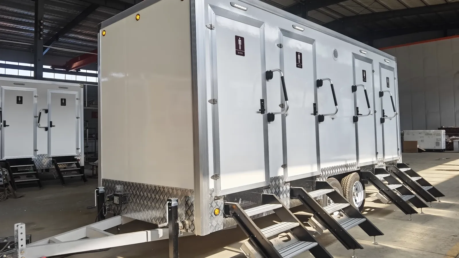 Exterior side view of a 4 stall restroom trailer showing door access, chassis, wheels, stabilizer jacks, and production finish.