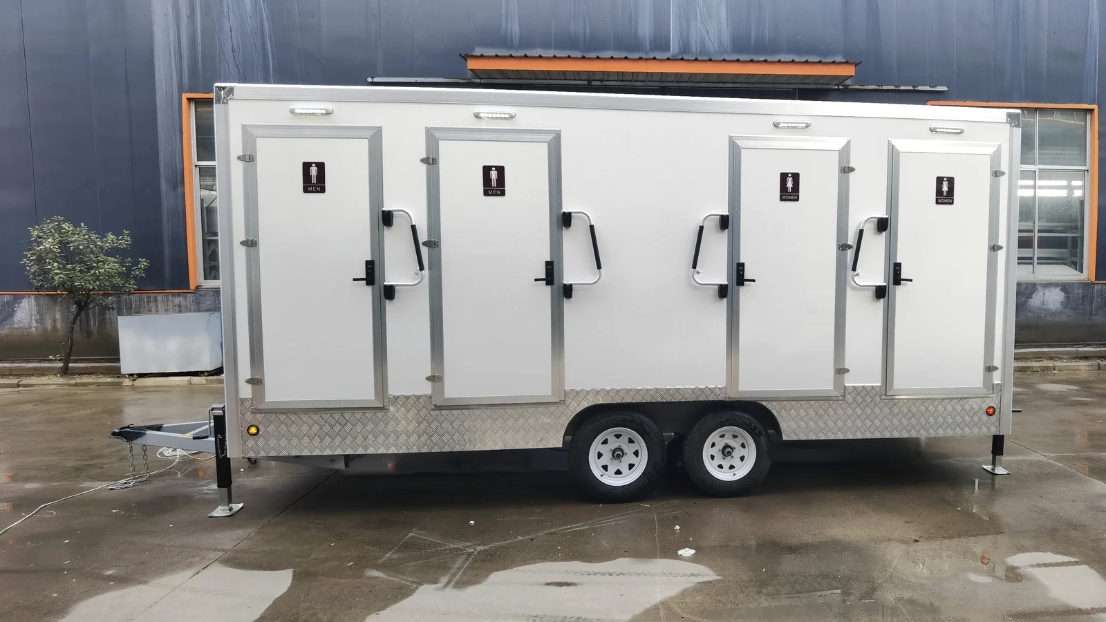 Side view of a 4 stall restroom trailer showing four private restroom doors, exterior handles, dual wheels, and stabilizer legs.
