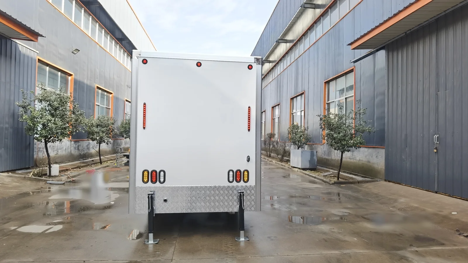 Rear view of a 4 stall restroom trailer showing tail lights, rear panel, stabilizer legs, and factory production finish.