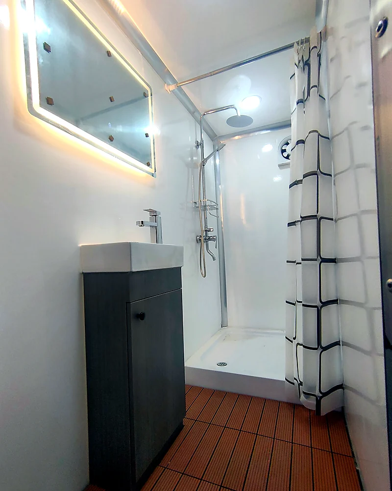 Private mobile shower trailer room with sink, mirror, shower fixture, curtain, waterproof wall panels, and easy-clean flooring.