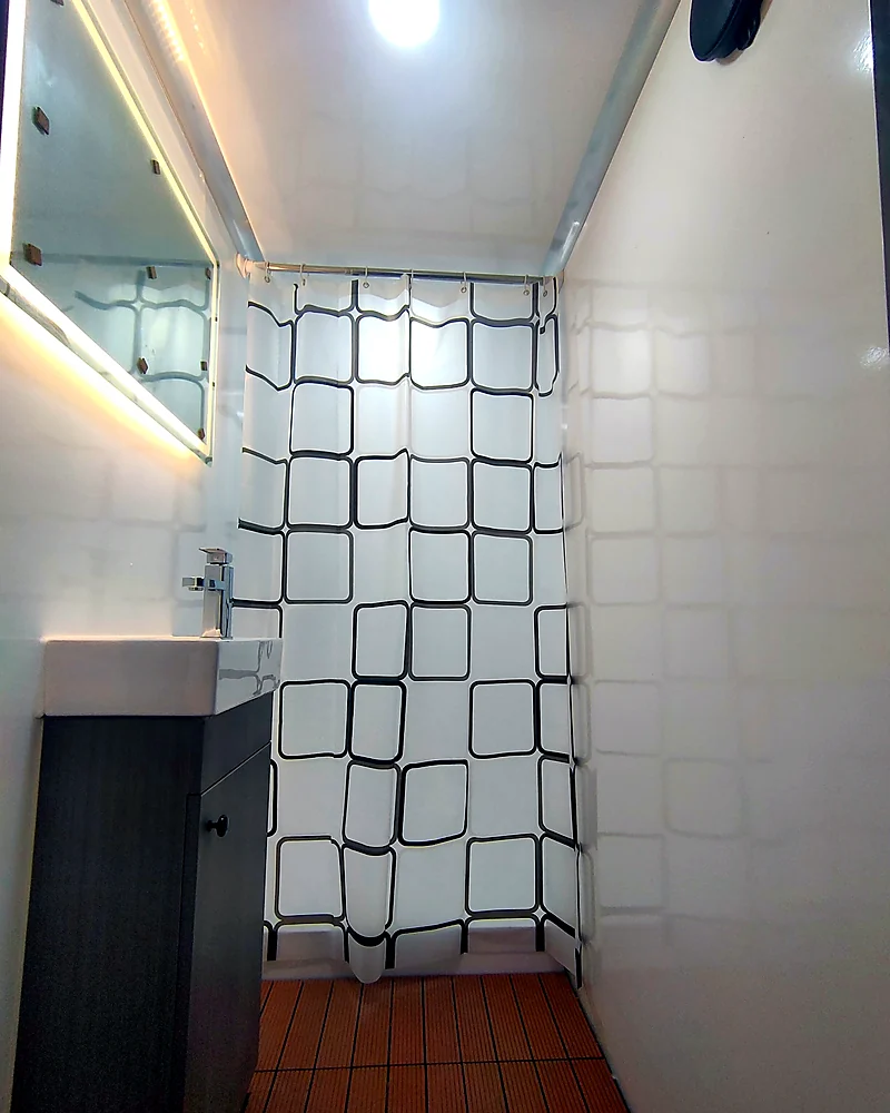 Mobile shower trailer changing area with vanity, mirror, waterproof wall panels, shower curtain, and private room layout.