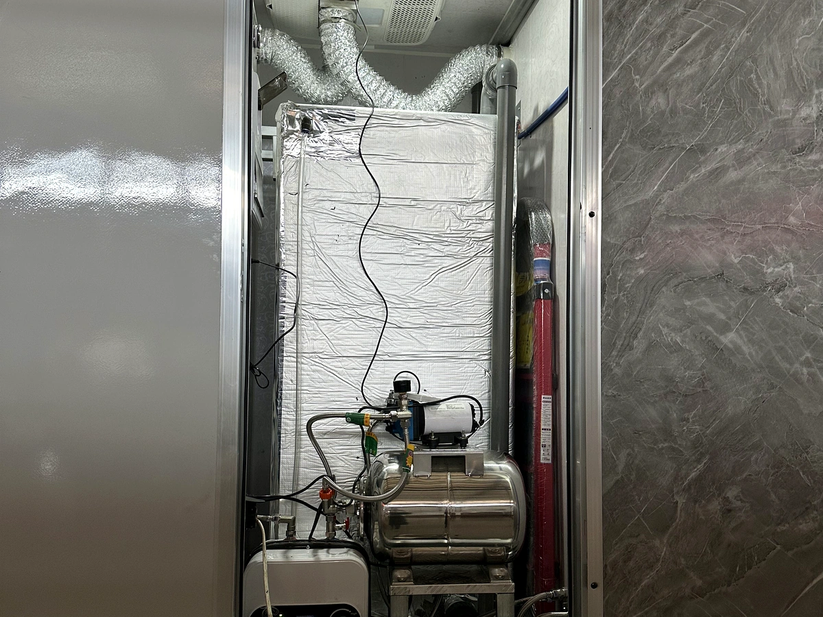 Utility room of an ADA restroom trailer showing pump, piping, ventilation, and service access compartment.