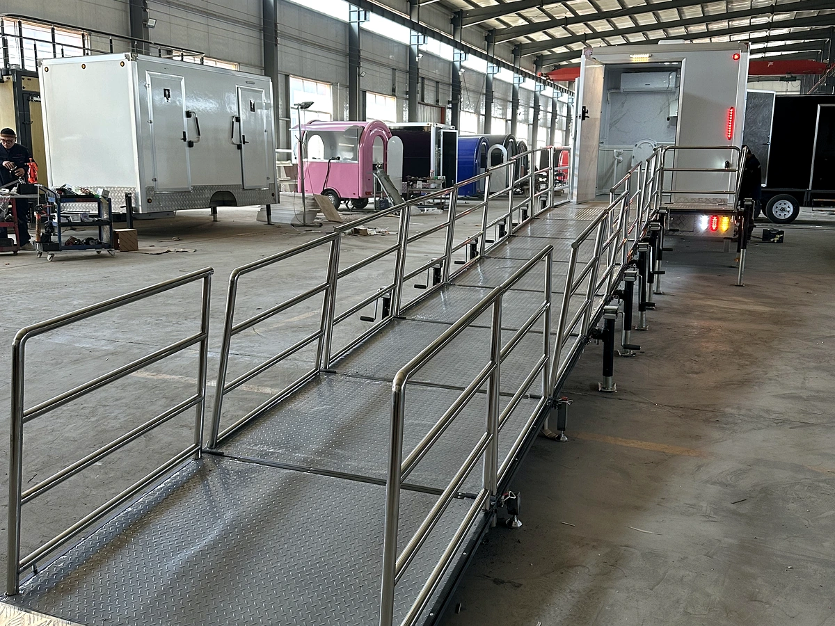 Long wheelchair ramp system connected to an ADA restroom trailer with stainless steel handrails and anti-slip aluminum deck.